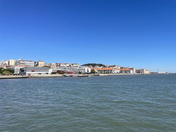 Buildings by sea against clear blue sky