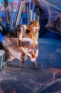 Full length of woman wearing ballet shoes while sitting in corridor of building 