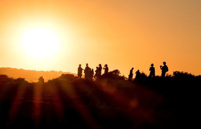 Silhouette friends on field against orange sky