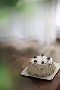 There is a delicious white cream blueberry birthday cake on the wooden table