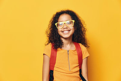 Portrait of young woman standing against yellow background