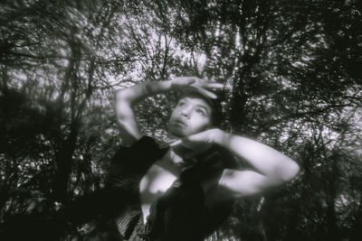 Low angle portrait of woman standing by tree in forest