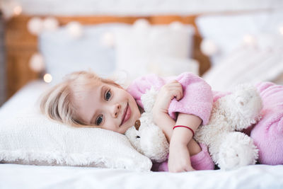 Cute girl with teddy bear lying on bed