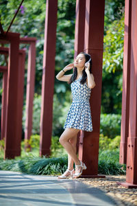 Full length of young woman listening music while standing in park