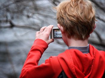 Rear view of boy photographing lake through digital camera