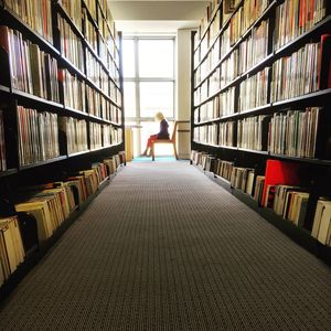 Woman sitting on chair amidst bookshelf in library