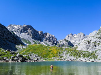 Rear view of shirtless man in lake against mountains and clear sky