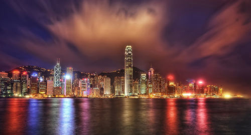 Illuminated city by river against sky at night