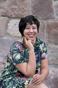 Portrait of smiling woman sitting against stone wall