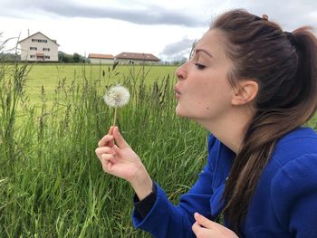 Portrait of young woman holding dandelion flower on field