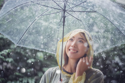 Woman with umbrella against trees during rainy season
