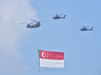 Low angle view of helicopter flying with flag against blue sky