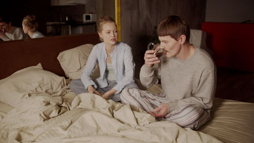 Man drinking coffee while sitting with girlfriend on bed