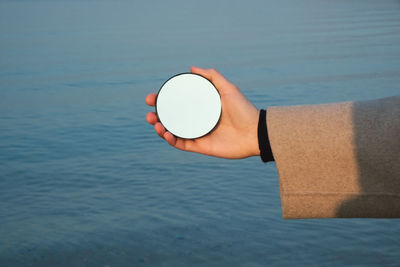 High angle view of arm holding round mirror on blue background