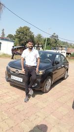 Portrait of smiling young man standing on car