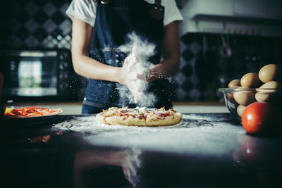 Midsection of woman preparing pizza in kitchen at home