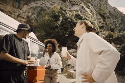 Happy multiracial male and female friends talking while having drinks during road trip