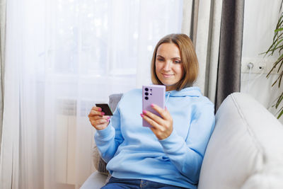 Young woman using mobile phone while sitting on bed at home