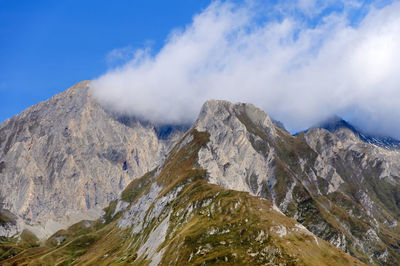 Low angle view of rocky mountains against cloudy sky