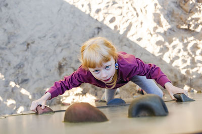 Girl with red hair climbing wall at playground