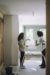 Female design professional discussing with customer while standing in under construction apartment