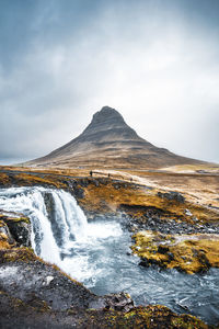 Scenic view of waterfall with mountain in background against cloudy sky