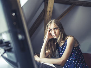 Thoughtful girl using computer while sitting on table