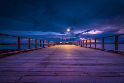 Empty footbridge over sea against sky at dusk
