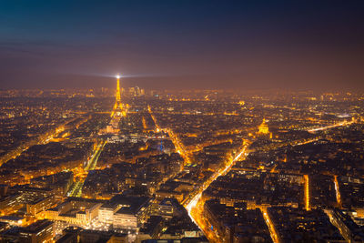 Aerial view of dark night sky above illuminated buildings and roads with high eiffel tower in district of paris