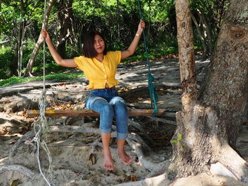 Full length portrait of a young woman sitting on tree trunk