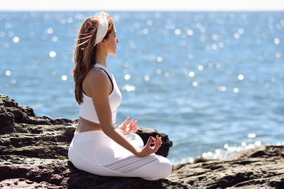 Side view of woman doing yoga on rock formation by sea