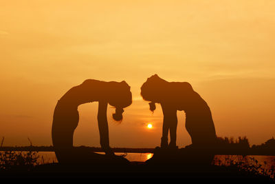 Silhouette of women doing yoga against sky during sunset