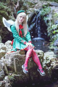 Full length of girl in angel costume sitting on rock