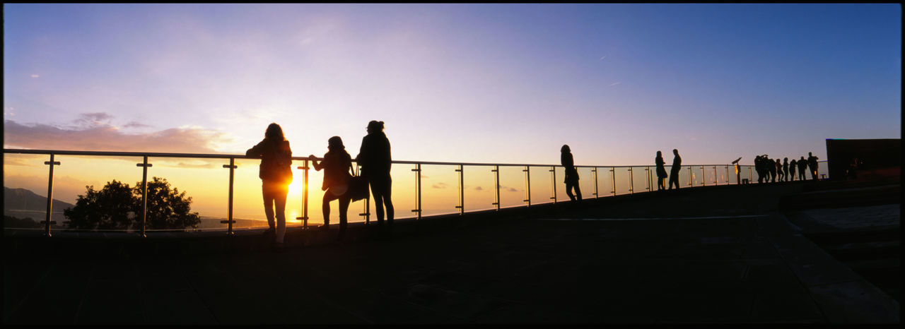 SILHOUETTE PEOPLE BY RAILING AGAINST SKY DURING SUNSET