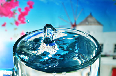 Close-up of drop splashing in drinking glass against sky