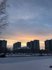 Snow covered buildings against sky during sunset