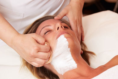 Midsection of beautician cleaning customer facial mask in spa