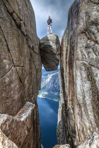 Low angle view of person standing on cliff against sky