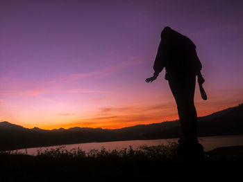 Silhouette person standing on shore against sky during sunset