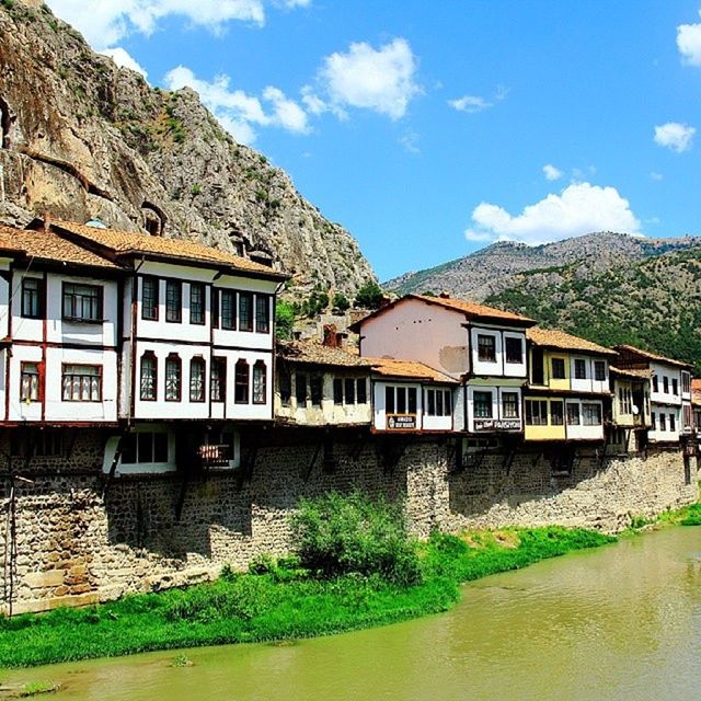 mountain, architecture, building exterior, built structure, water, sky, house, mountain range, reflection, residential structure, waterfront, tree, day, transportation, river, nature, canal, residential building, lake, window