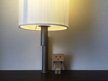 Close-up of electric lamp by figurine on table against wall at home