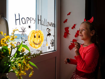 Child painting pumpkin window preparing celebrate halloween kid draws decorates room with paper bats