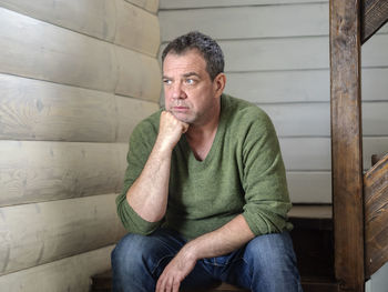 Thoughtful man sitting on wooden seat at home