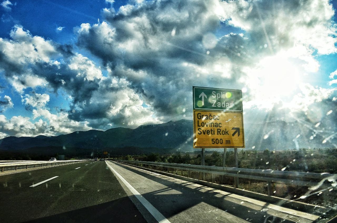 sky, text, transportation, cloud - sky, western script, communication, mountain, road, cloud, road sign, landscape, information sign, cloudy, sign, mode of transport, warning sign, guidance, mountain range, nature, scenics