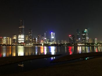 Illuminated buildings by river against sky at night