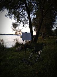 Chair on field by lake against sky