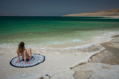 Woman sitting on shore at beach against sky