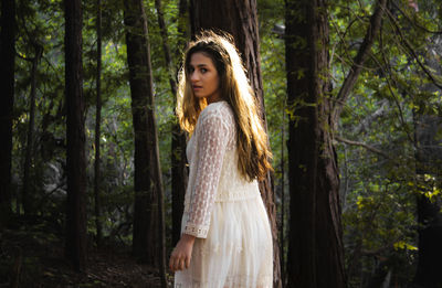Portrait of beautiful woman in white dress standing in forest