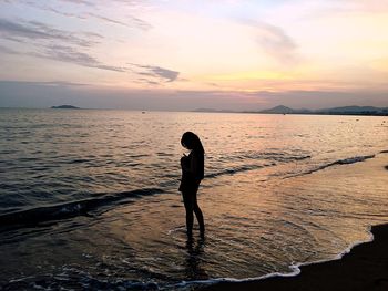 Silhouette woman standing at beach against sky during sunset