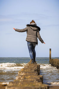 Rear view of woman walking on wooden posts in sea against sky